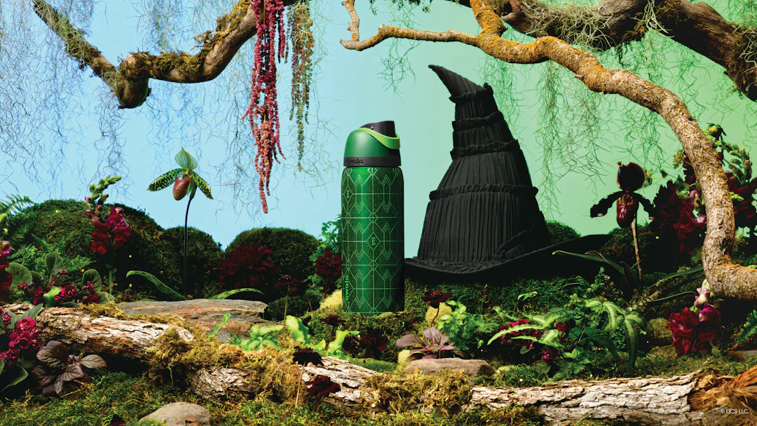 Shot of green water bottle next to the official hat from the movie, in a forest-inspired scene